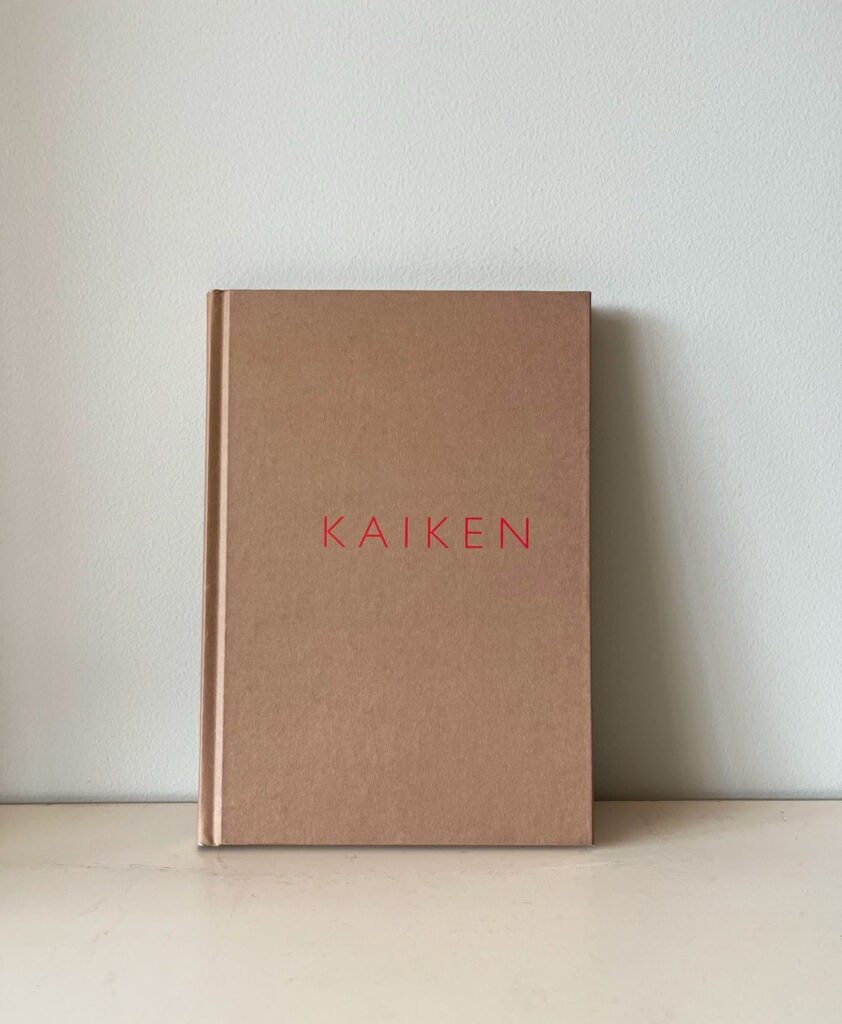 Kuvassa Petra Vallilan teos kaiken. Kirjassa on vaalenruskea kansi ja siinä lukee punaisella KAIKEN. Kirja on vaalealla tasolla ja se nojaa vasten vaaleaa seinää.